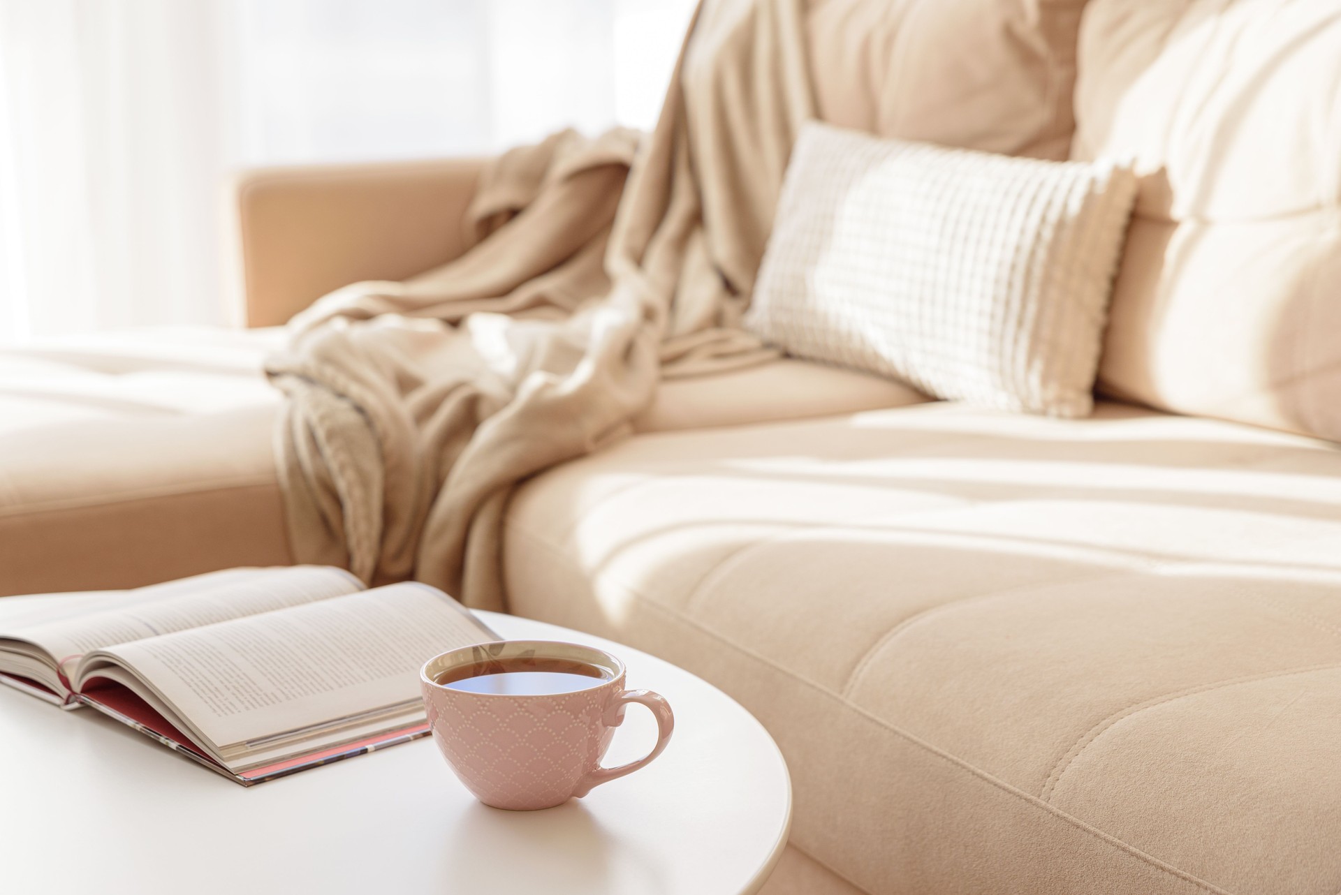 Cozy living room with a book and tea on a beige couch. Soft focus